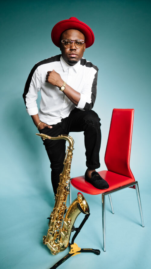 A man sitting on top of a red chair next to a saxophone.