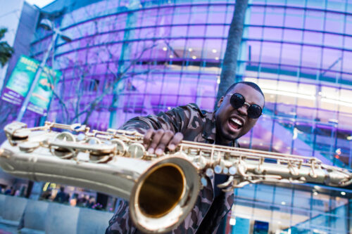 A man holding a saxophone in front of a building.