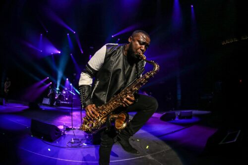 A man with a saxophone in front of purple lights.