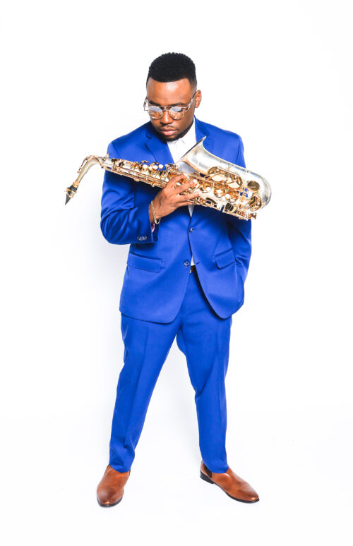 A man in blue suit and glasses holding a saxophone.