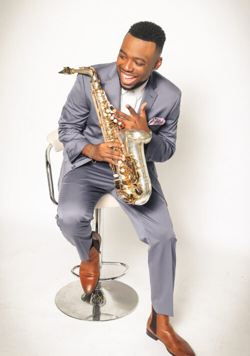 A man in grey suit holding a saxophone.
