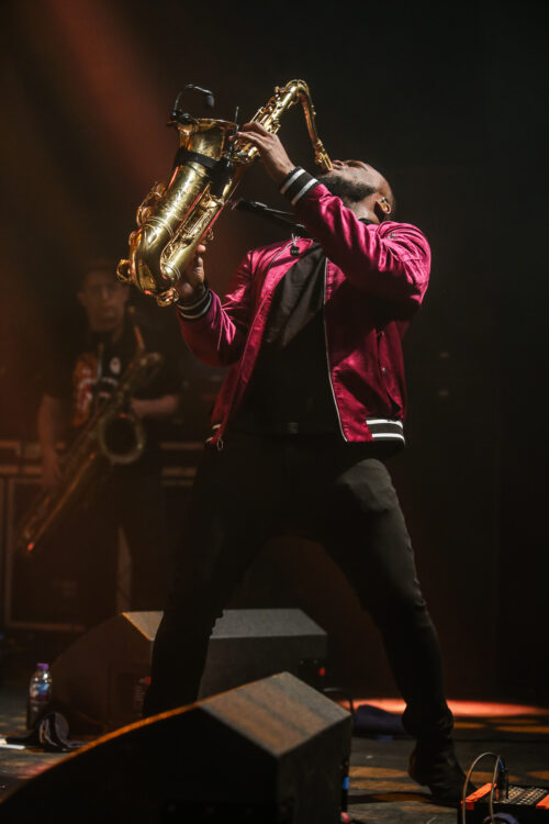 A man playing the saxophone on stage with other musicians.